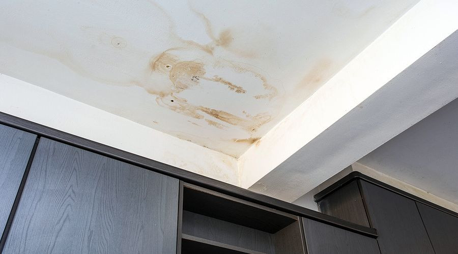 Damaged ceiling with stains and wooden wall cabinets in a residential space needing plumbing attention.
