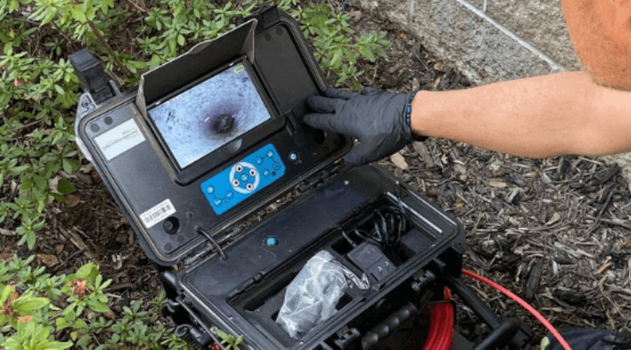 Technician using portable inspection camera for plumbing, showing detailed screen image of pipes.