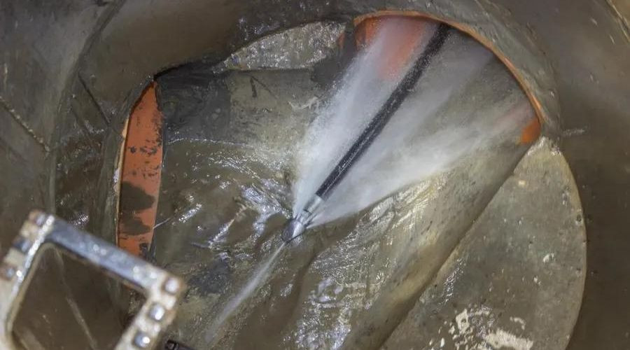 High-pressure water jet nozzle for plumbing maintenance, showcasing water ejection and debris around the opening.