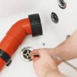 Hands of a plumber working on red plastic pipe and drain assembly with tools for maintenance services.