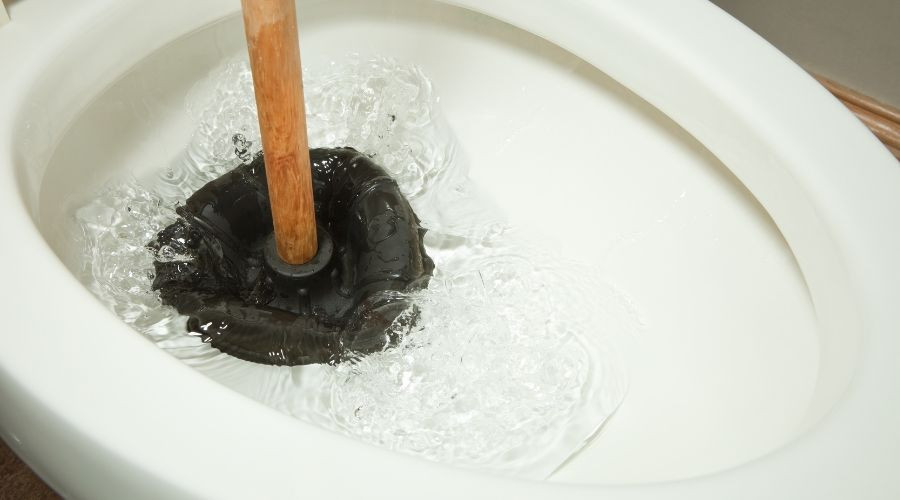 Black rubber plunger beside a white toilet bowl, illustrating essential plumbing maintenance for Super Plumbers.