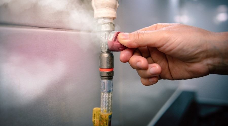 Hand adjusting a gas valve on a pipe, with steam visibly escaping, highlighting gas leak detection and safety measures.