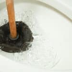 Plunger in toilet bowl creating bubbles, illustrating common tool for unclogging toilets and addressing sewer line issues.